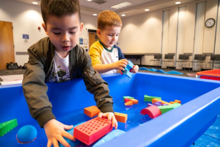 Two children play with toys in a water tub