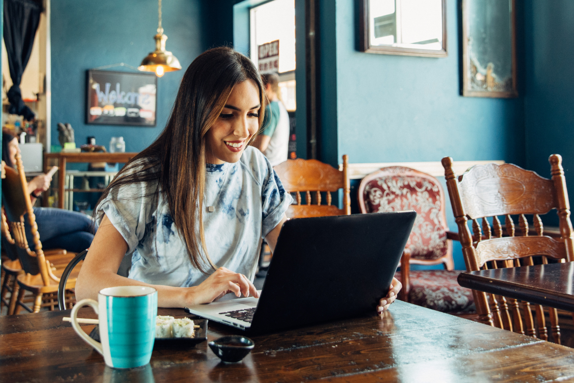 Young hispanic woman sits at a cafe table using her laptop
