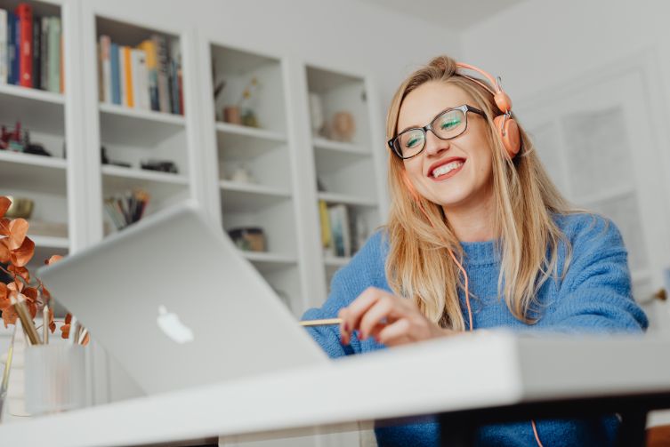 A young woman with headphones smiles as she works on her laptop.